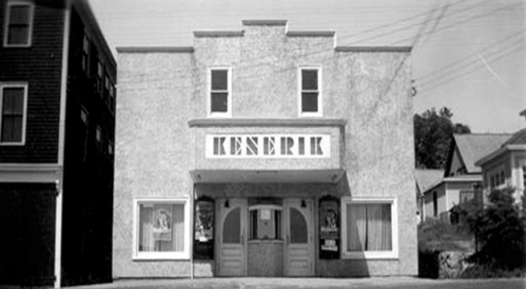 A black and white photo of a two story building. there is a box office ticket window out front and the sign reads Kenerik.