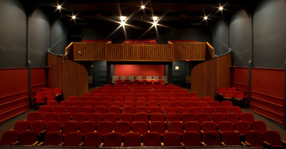 Interior image of the old playhouse auditorium. Red seats, back walls, and wood siding along the stairs to the balcony.